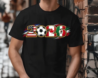 Może przedstawiać: Czarny t-shirt z numerem "2026" i piłką nożną. Projekt zawiera flagi Stanów Zjednoczonych, Kanady i Meksyku, sugerując motyw sportowy.