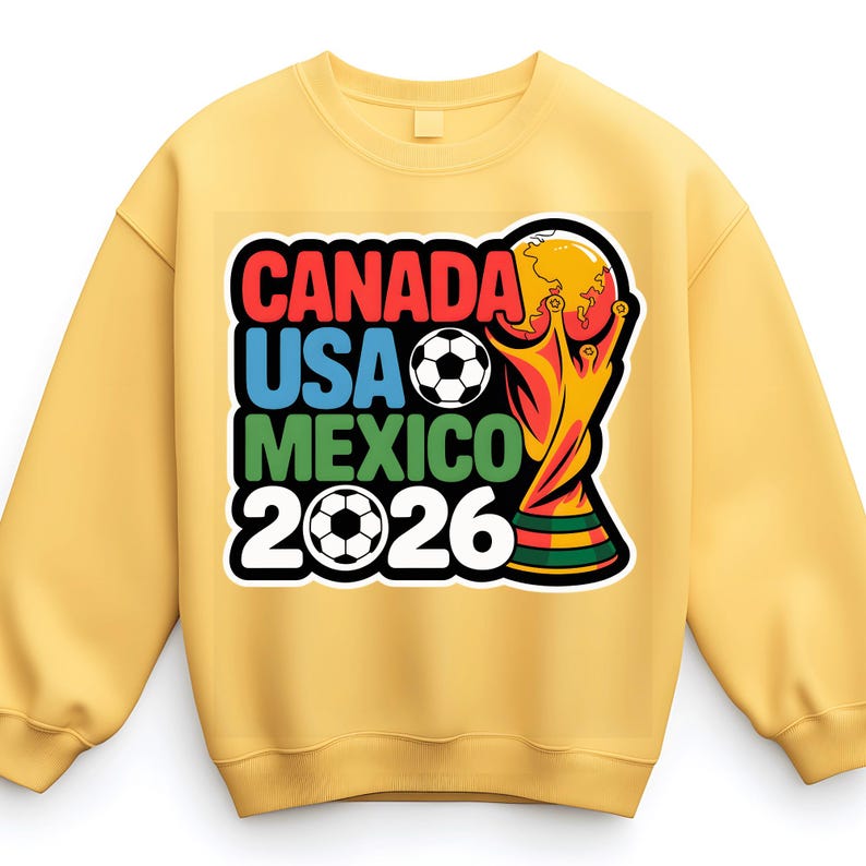 以下が含まれることがあります： 「CANADA USA MEXICO 2026」の文字がカラフルなデザインでプリントされたイエローのスウェットシャツ。サッカーボールとトロフィーのグラフィックが特徴です。スウェットシャツは無地のイエローです。
