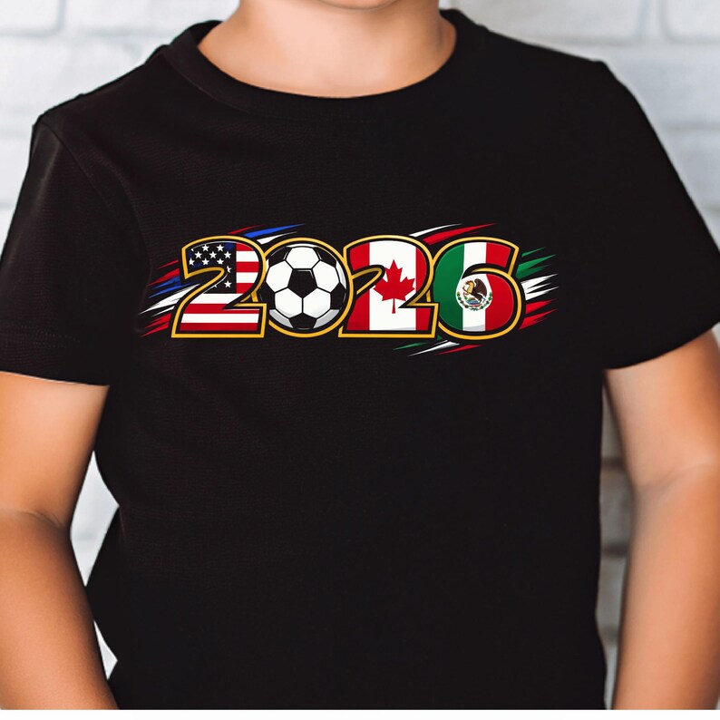Puede incluir: Camiseta negra con el a&ntilde;o "2026" y un bal&oacute;n de f&uacute;tbol en el centro. Los n&uacute;meros est&aacute;n dise&ntilde;ados con las banderas de Estados Unidos, Canad&aacute; y M&eacute;xico, con detalles en rojo, blanco, azul, verde y dorado.