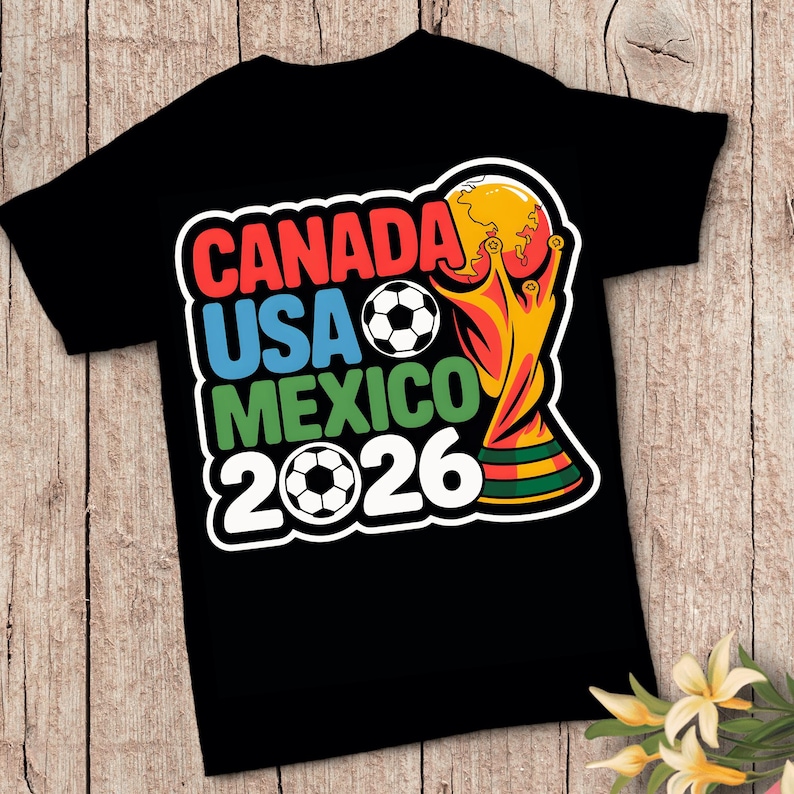 以下が含まれることがあります： 2026 FIFAワールドカップを宣伝するカラフルなグラフィックがプリントされた黒いTシャツ。「CANADA USA MEXICO 2026」の文字が赤、青、緑でデザインされ、サッカーボールとトロフィーが描かれています。