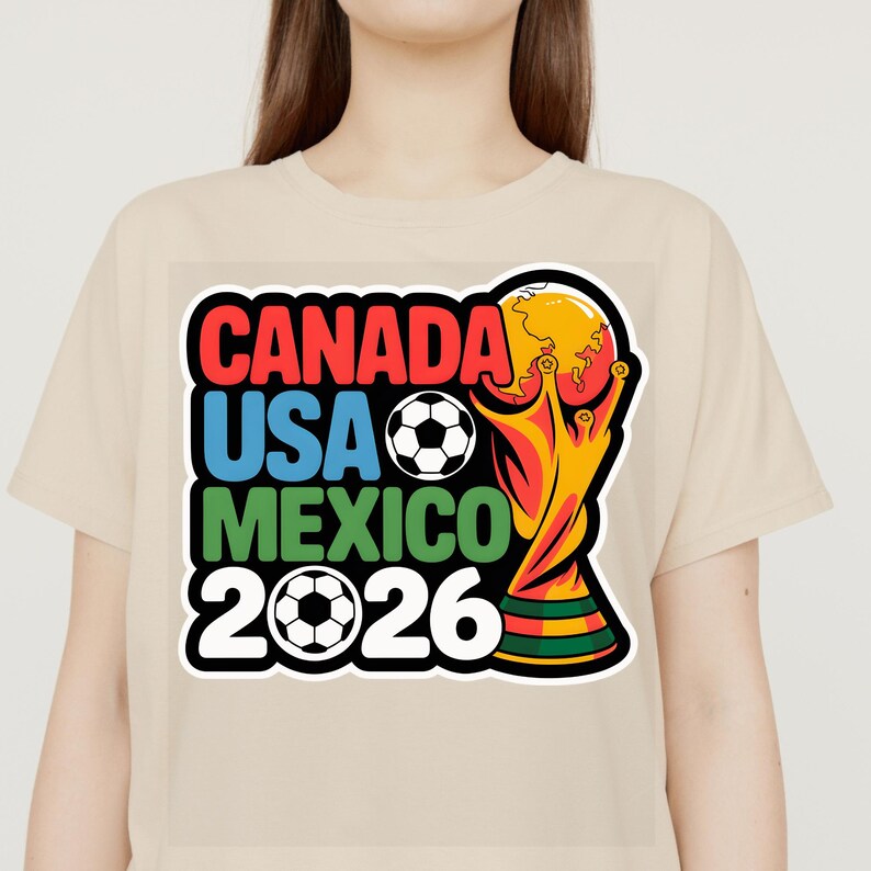 以下が含まれることがあります： 2026 FIFAワールドカップのカラフルなグラフィックがプリントされたベージュ色のTシャツ。「CANADA」「USA」「MEXICO」の文字が赤、青、緑でデザインされ、サッカーボールと「2026」の文字が描かれています。金色のトロフィーも表示されています。