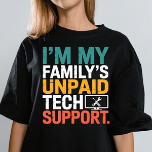 Könnte beinhalten: Schwarzes T-Shirt mit dem Text "I'M MY FAMILY'S UNPAID TECH SUPPORT." Der Text ist in Teal, Weiß, Gelb und Orange gehalten. Ein Computerbildschirm-Symbol mit einem Schraubenschlüssel ist ebenfalls enthalten.