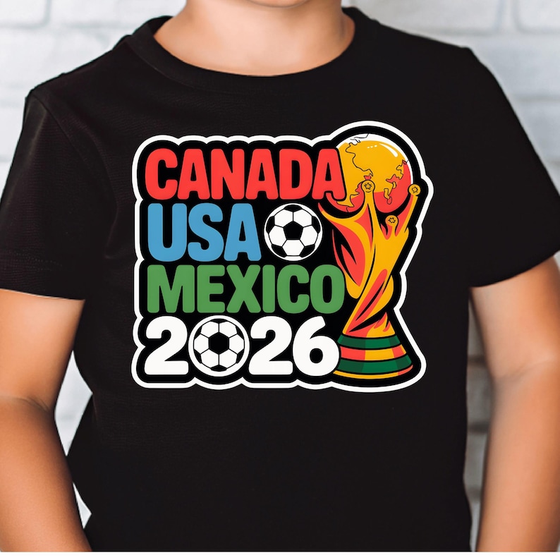 以下が含まれることがあります： 2026 FIFAワールドカップのカラフルなグラフィックがプリントされた黒いTシャツ。「CANADA USA MEXICO 2026」の文字が赤、青、緑、白でデザインされ、サッカーボールとトロフィーが描かれています。