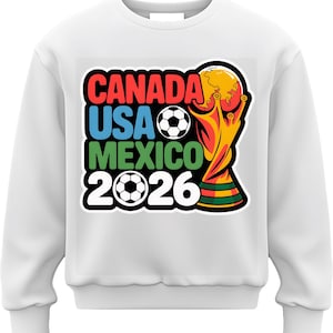 以下が含まれることがあります： 2026 FIFAワールドカップのグラフィックがプリントされた白いスウェットシャツ。「CANADA USA MEXICO 2026」の文字が赤、青、緑、白でデザインされています。サッカーボールとトロフィーも含まれています。