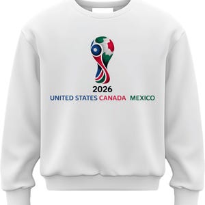 May include: White sweatshirt featuring the 2026 FIFA World Cup logo. The logo is a stylized design with red, blue, and green elements, and the text "2026" is below it. The words "UNITED STATES CANADA MEXICO" are printed in blue, green, and red.