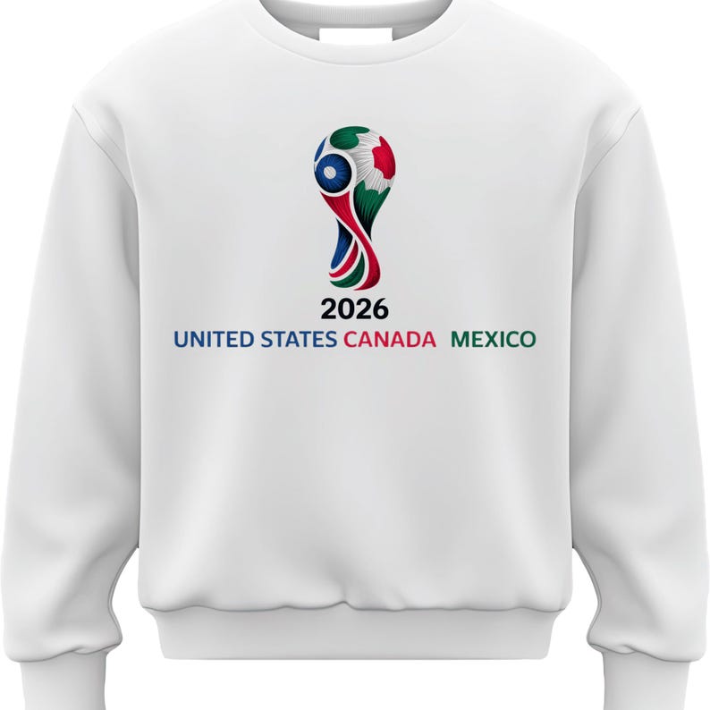 May include: White sweatshirt featuring the 2026 FIFA World Cup logo. The logo is a stylized design with red, blue, and green elements, and the text "2026" is below it. The words "UNITED STATES CANADA MEXICO" are printed in blue, green, and red.