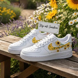May include: White sneakers with yellow sunflower designs on a wooden bench in a garden setting. The sneakers have a yellow swoosh and sunflower accents. A sign that says "Step into Sunshine" is also in the image.