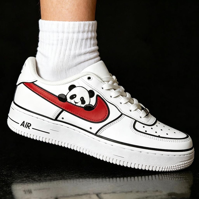 May include: White leather sneaker with a red swoosh and a panda bear graphic. The shoe has black accents and the word "AIR" printed on the side. The sneaker is a low-top style.