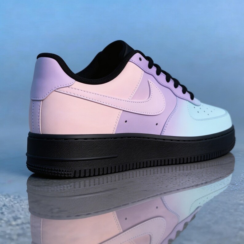 Op de afbeelding: Een pastelkleurige sneaker met een zwarte zool. De schoen heeft een gradi&euml;ntontwerp, dat overgaat van roze naar paars naar lichtblauw. De iconische Nike swoosh is zichtbaar aan de zijkant. De schoen wordt weerspiegeld in het oppervlak eronder.