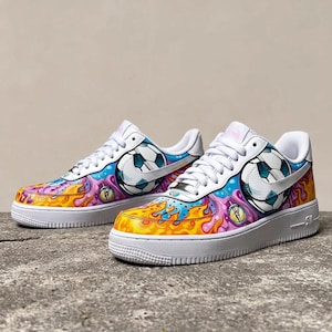 May include: Pair of white sneakers with a colorful design featuring a soccer ball, flames, and abstract shapes in yellow, orange, blue, and purple. The shoes have white laces and soles.