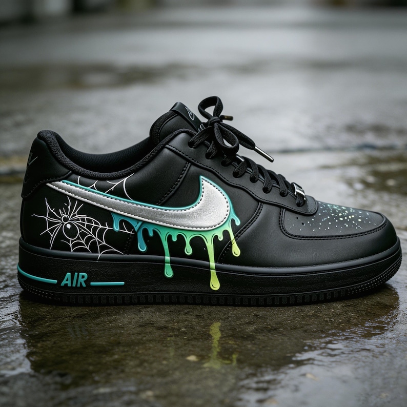 May include: Black Air Force 1 sneakers with a custom design. The shoe features a silver Nike swoosh, a spiderweb graphic, and dripping paint in shades of blue and green. The word "AIR" is printed in teal.