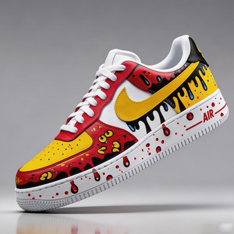 Puede incluir: Una zapatilla Air Force 1 personalizada. La zapatilla presenta una puntera amarilla, superposiciones rojas y un panel central blanco con un swoosh amarillo. Gotas negras y salpicaduras rojas a&ntilde;aden un toque art&iacute;stico &uacute;nico. La palabra "AIR" est&aacute; impresa en el lateral.