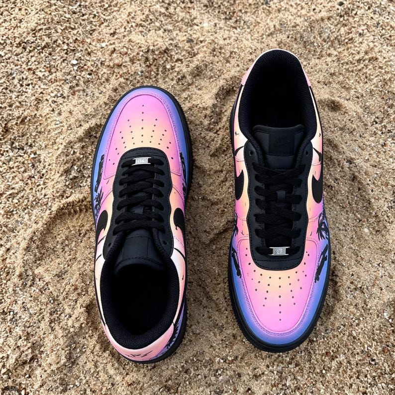 May include: Pair of black and iridescent sneakers with a gradient of pink, orange, and blue hues. The sneakers feature black laces, a black tongue, and a black swoosh logo. The shoes are on a sandy surface.