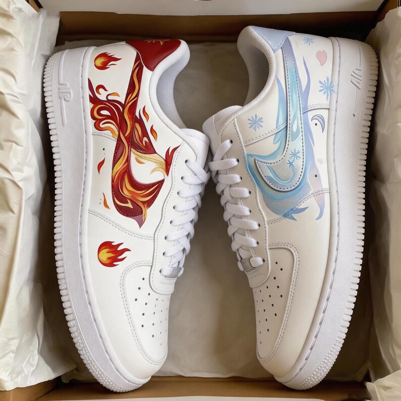 May include: Pair of white sneakers with custom artwork. One shoe features a fiery phoenix design in red, orange, and yellow. The other shoe has a blue and white snowflake theme with a light blue swoosh. The shoes are in a cardboard box.