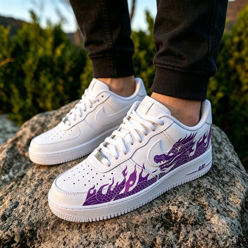 May include: White leather sneakers with a purple dragon design on the side. The sneakers have a classic low-top design with a white sole and laces. The Nike swoosh is visible on the side. The word "AIR" is printed on the side.
