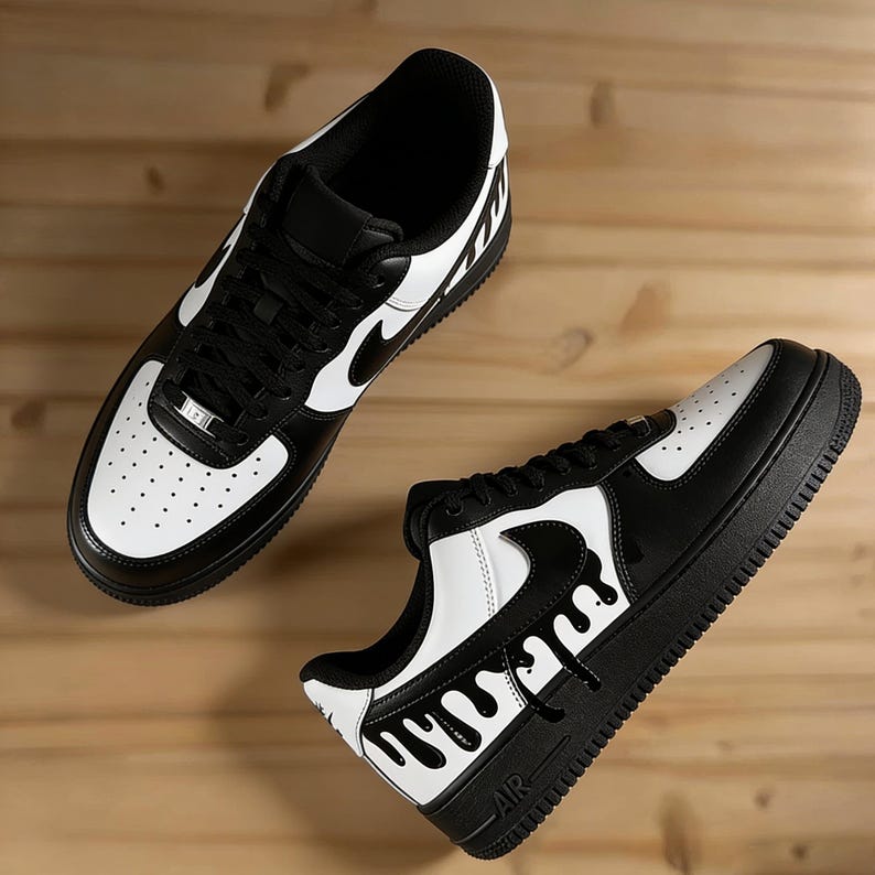 May include: Pair of black and white sneakers with a unique drip design on the side. The shoes feature a black sole, white accents, and the iconic Nike swoosh logo. The sneakers are displayed on a wooden surface.
