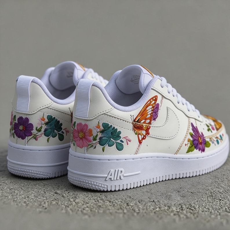 May include: Off-white sneakers with floral and butterfly embroidery. The low-top shoes feature colorful flowers in purple, pink, and teal, and a large orange butterfly. The white soles have the word "AIR" on the side.
