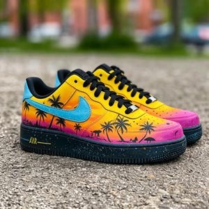 May include: A pair of custom-painted sneakers featuring a tropical sunset design. The shoes have a yellow, orange, and pink gradient with black palm tree silhouettes. A blue swoosh and black sole complete the design.