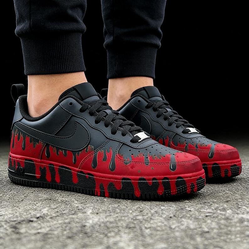 May include: Black and red sneakers with a unique dripping paint design. The shoes feature a black upper with a red, dripping paint effect on the lower portion and sole. The Nike swoosh is visible on the side.