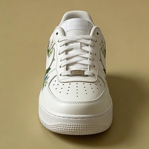 May include: White leather trainer with floral design accents. The shoe features white laces, a white sole, and a small metal tag on the laces. The floral design includes green, yellow, and blue flowers.