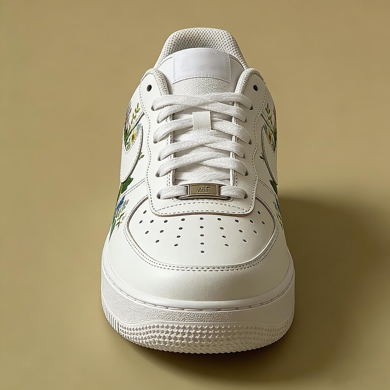 May include: White leather trainer with floral design accents. The shoe features white laces, a white sole, and a small metal tag on the laces. The floral design includes green, yellow, and blue flowers.