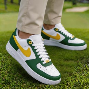 May include: White, green, and yellow sneakers with white laces. The sneakers have a green toe and heel, a yellow swoosh, and a white sole. The shoes are on a green grassy surface.