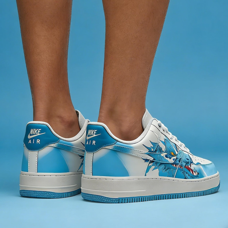 May include: White and blue Nike Air Force 1 sneakers with a dragon graphic on the side. The sneakers have a white sole and blue accents on the heel and side panels. The Nike Air logo is visible on the heel.