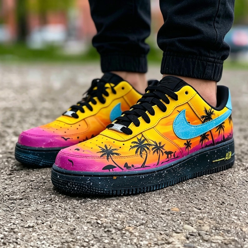 May include: Customized sneakers with a vibrant sunset design. The shoes feature a gradient of yellow, orange, and pink, with black palm tree silhouettes. A light blue swoosh and black laces complete the look. The black sole has white speckles.