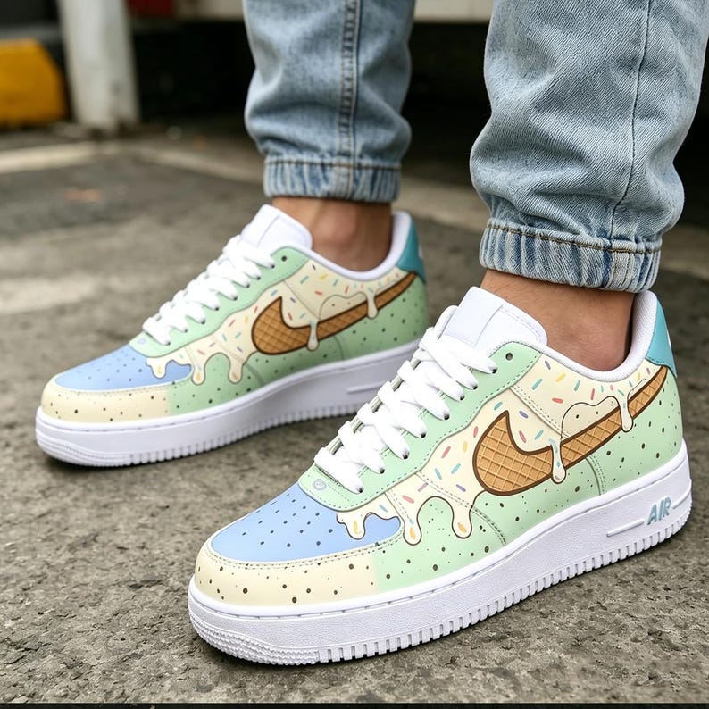 May include: Custom Nike Air Force 1 sneakers with a unique ice cream cone design. The shoes feature a white sole, blue and green panels, and a brown waffle cone swoosh with colorful sprinkles. White laces complete the look.