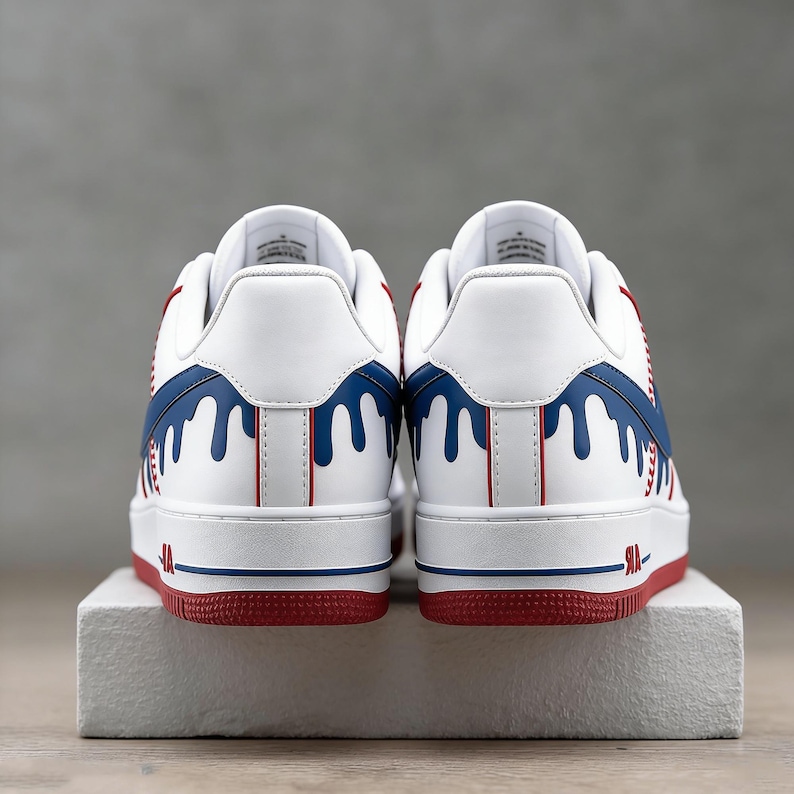 May include: White sneakers with red and blue accents. The design features a white base with blue dripping paint details and red accents on the sole and heel. The sneakers are displayed on a white block.