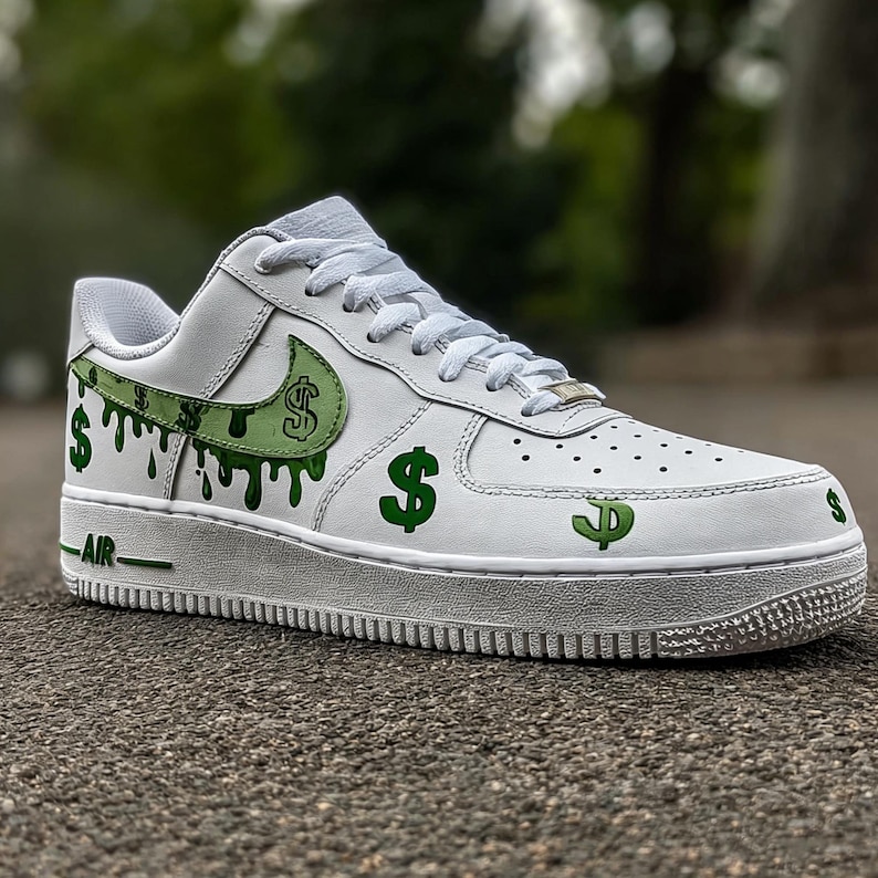 May include: White leather trainer with green dollar sign graphics and dripping paint design. The shoe features a white sole and laces, with the word "AIR" in green on the side. A unique and stylish footwear option.