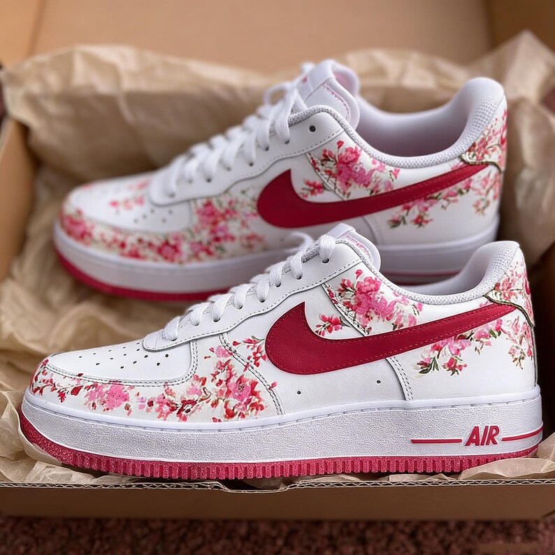 May include: White trainers with a floral pattern. The shoes have a white base, adorned with pink floral designs and a red swoosh. The soles are white with a red trim, and the word "AIR" is visible on the side.