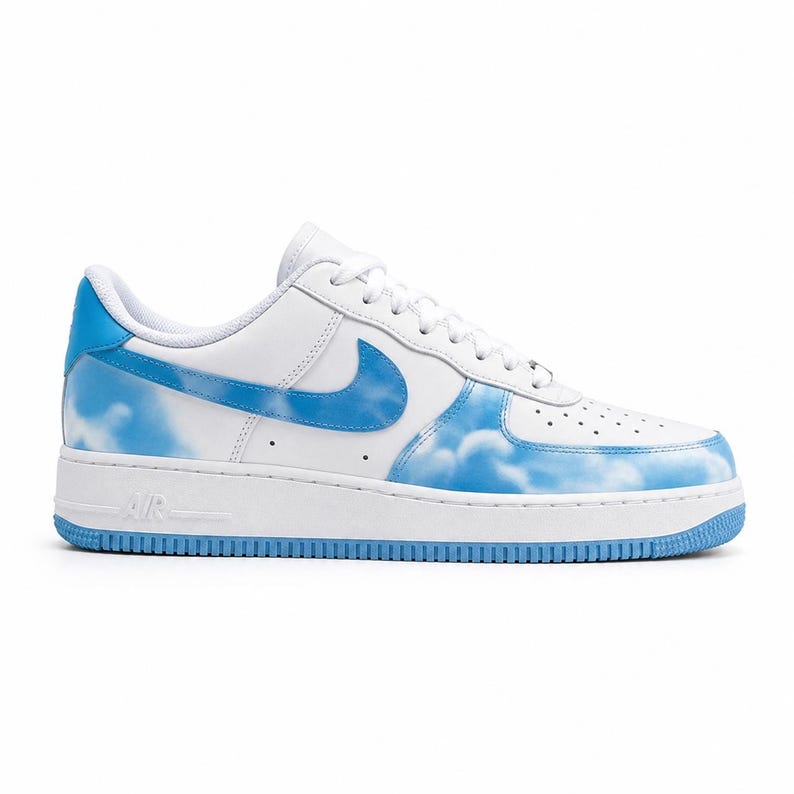 May include: White and blue Air Force 1 sneakers with a cloud design. The sneakers feature a white leather upper with blue accents on the Swoosh, heel, and sole. The cloud pattern is painted on the toe and side panels.