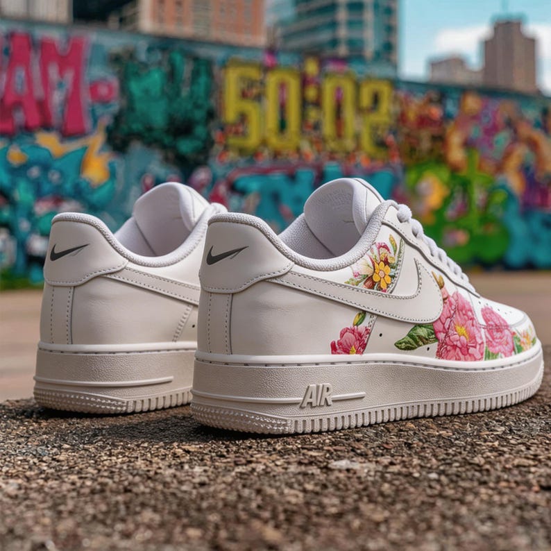 May include: Pair of white trainers featuring floral patterns in pink, yellow, and green. The shoes have a beige sole and the word "AIR" is visible. A black Nike swoosh logo is on the side and heel.