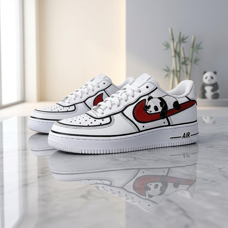 May include: White sneakers with a panda bear design. The shoes feature a red swoosh with a panda graphic, black trim, and the word "AIR" on the midsole. The sneakers are on a reflective surface.