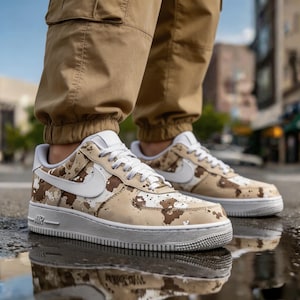 May include: A pair of Air Force 1 sneakers in a desert camouflage pattern. The shoes have a white sole, white laces, and a white Nike swoosh. The sneakers are worn with tan cargo pants.