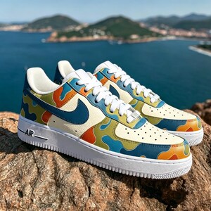 May include: A pair of colorful sneakers with a cream-colored base and a vibrant pattern of orange, blue, and green shapes. The shoes have a white sole and laces, with a blue Nike swoosh. The word "AIR" is printed on the side.