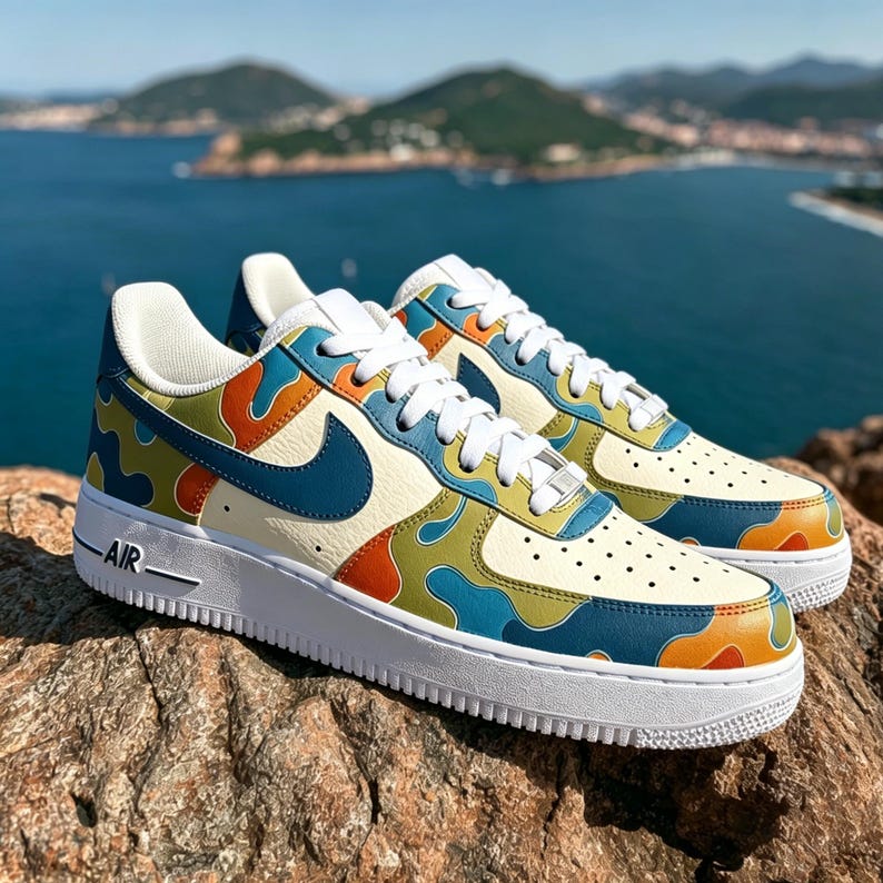 May include: A pair of colorful sneakers with a cream-colored base and a vibrant pattern of orange, blue, and green shapes. The shoes have a white sole and laces, with a blue Nike swoosh. The word "AIR" is printed on the side.