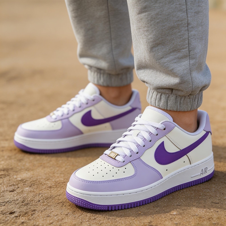 May include: White and lavender sneakers with a purple swoosh logo. The shoes have a white sole and a purple outsole. The word "AIR" is printed on the side of the sole. The sneakers are worn with gray sweatpants.