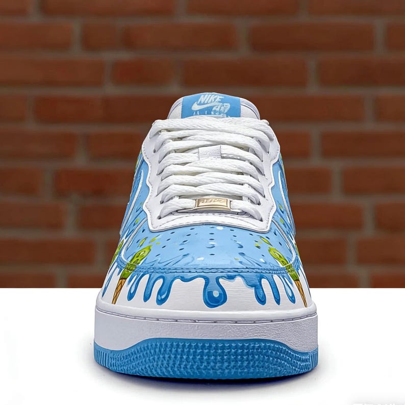 Puede incluir: Zapatillas Nike Air Force 1 blancas con dise&ntilde;o personalizado de conos de helado azules y verdes. La zapatilla tiene suela, cordones y leng&uuml;eta blancos, con el logo de Nike en la leng&uuml;eta. El dise&ntilde;o incluye pintura azul goteando.