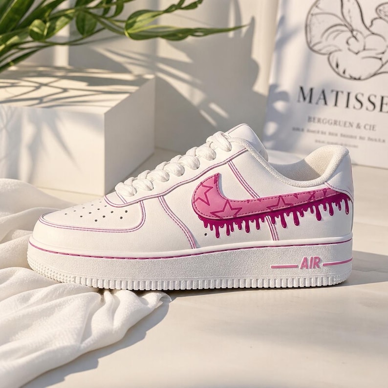 May include: White athletic shoe with a pink star design on the side. The shoe features pink accents, including the outline, sole, and the word "AIR". The design includes a dripping paint effect.