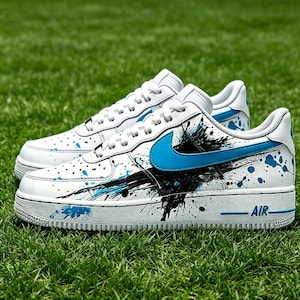 May include: White sneakers with blue accents and a black splatter design. The shoes feature a blue swoosh logo and the word "AIR" in blue on the side. The sneakers are on a green grass background.