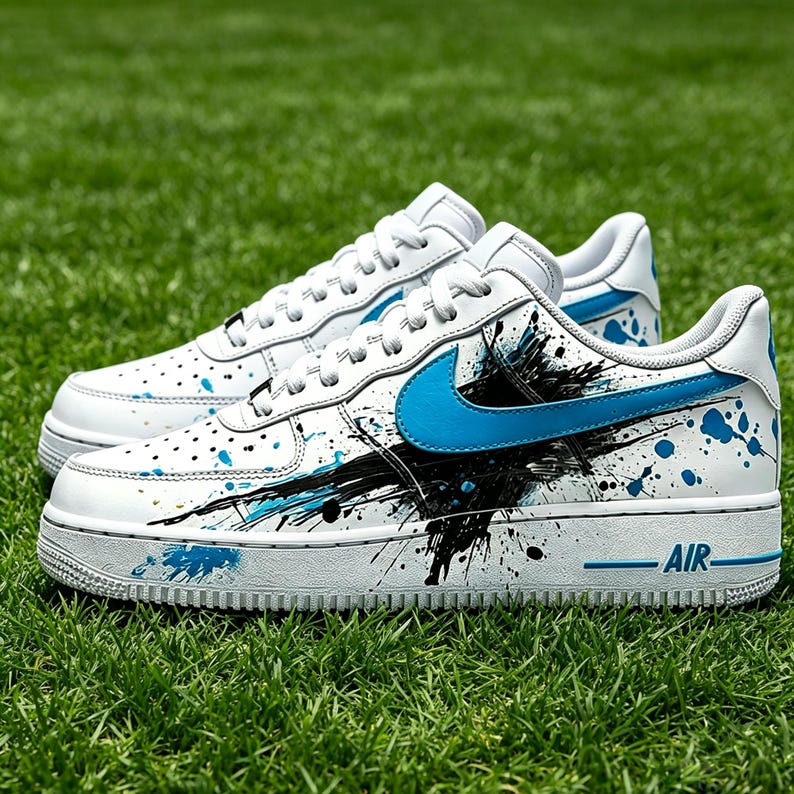 May include: White sneakers with blue accents and a black splatter design. The shoes feature a blue swoosh logo and the word "AIR" in blue on the side. The sneakers are on a green grass background.