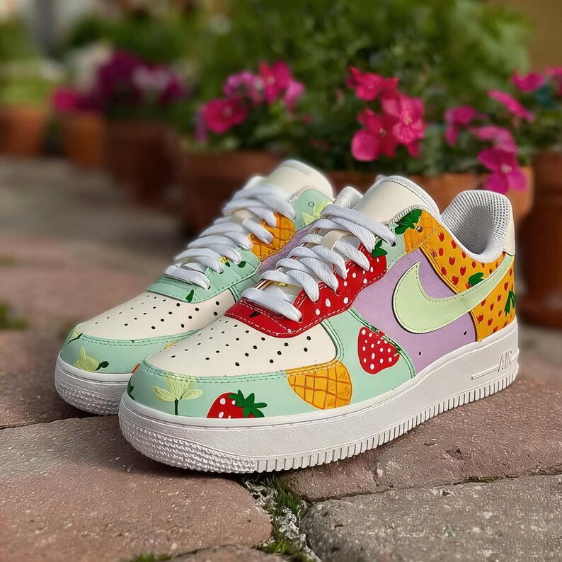 Puede incluir: Zapatillas blancas personalizadas con un dise&ntilde;o de frutas colorido. Los zapatos presentan fresas, pi&ntilde;as y otros patrones de frutas sobre una base blanca con un swoosh verde claro. Las suelas son blancas.