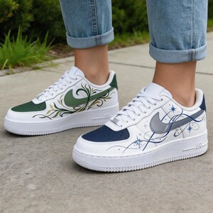 May include: White sneakers with custom designs. One shoe features a green and gold floral pattern, while the other has a navy blue toe and a silver swoosh with blue star and line accents. The shoes have white soles.