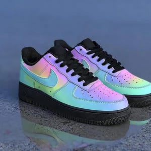 May include: Pair of iridescent sneakers with a black sole, laces, and tongue. The sneakers feature a gradient of colors, including blue, green, and pink. The Nike swoosh is visible on the side.