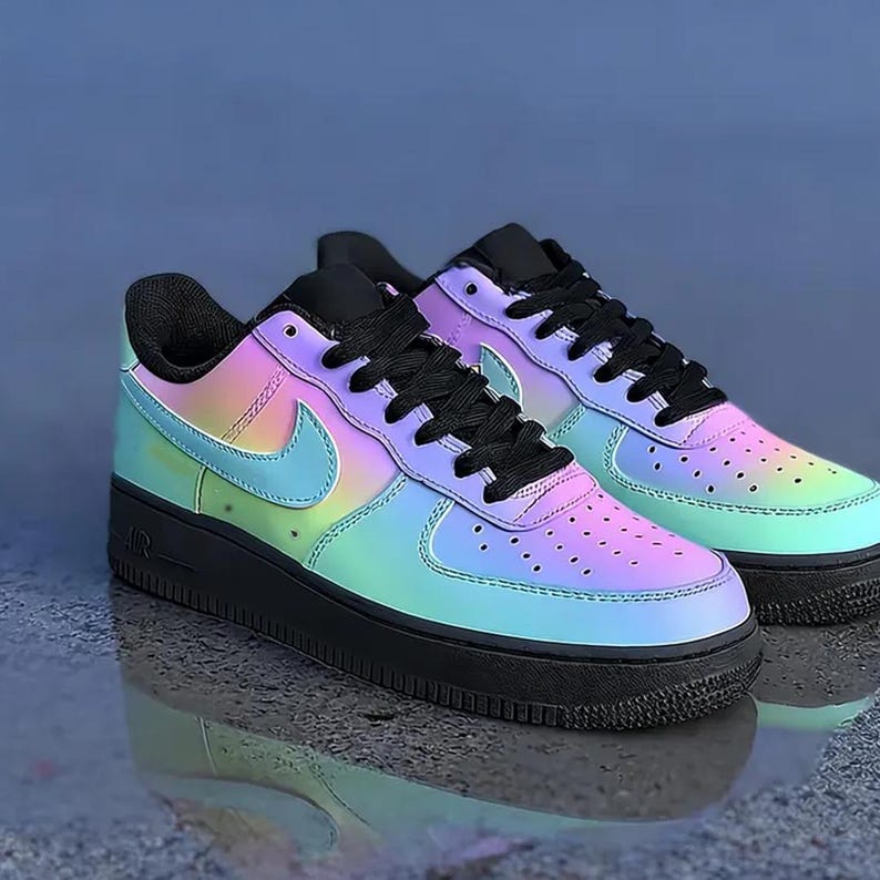 May include: Pair of iridescent sneakers with a black sole, laces, and tongue. The sneakers feature a gradient of colors, including blue, green, and pink. The Nike swoosh is visible on the side.