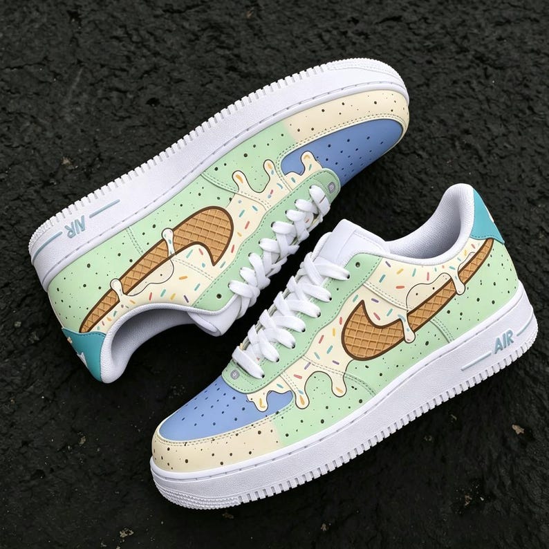 May include: Pair of custom Nike Air Force 1 sneakers with a unique ice cream cone design. The shoes feature a white sole, light blue, green, and yellow accents, and a brown waffle cone-shaped Nike swoosh with colorful sprinkles.