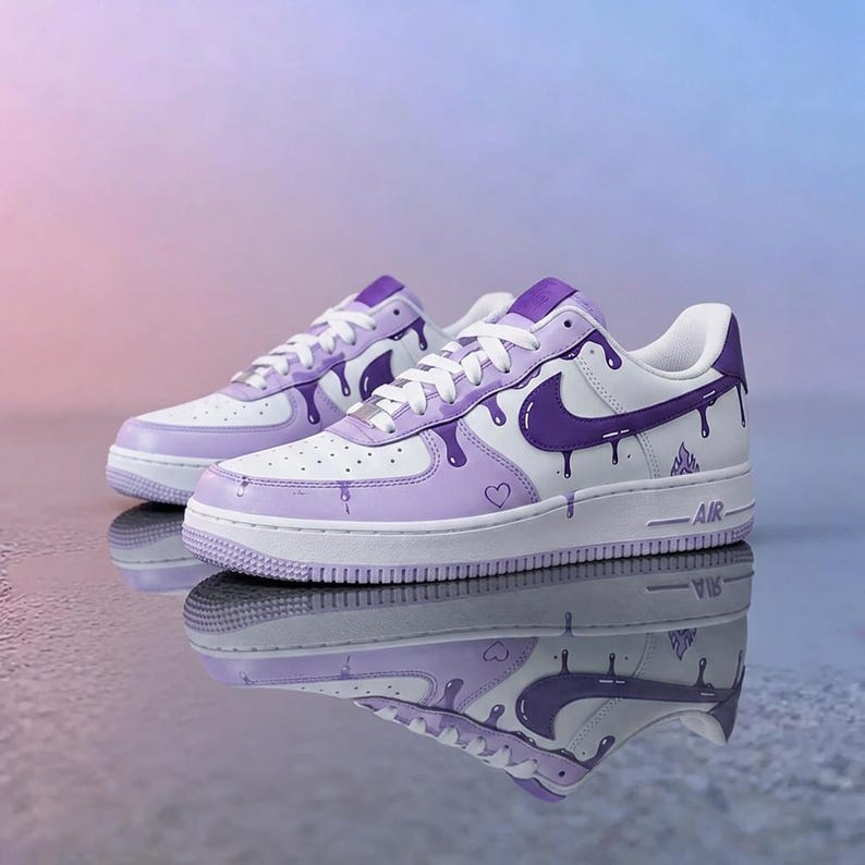 May include: White and lavender Air Force 1 sneakers with purple drip design. The sneakers have a white sole, white laces, and a purple Nike swoosh. A small heart is visible on the side of the shoe.