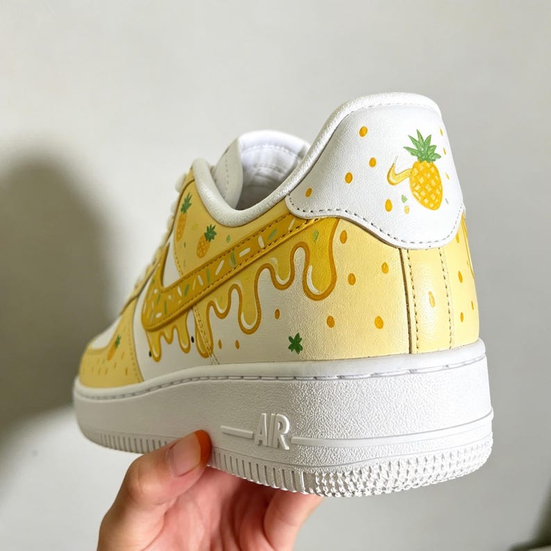 May include: White and yellow custom sneakers with a pineapple theme. The shoes feature a white base with yellow accents, including a dripping design and pineapple illustrations. The sole is white, and the design includes green star accents.